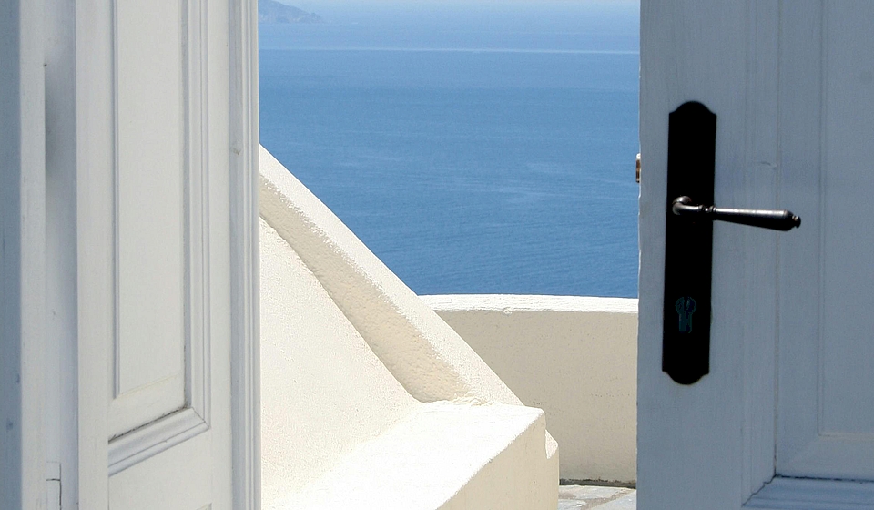 Eine offene Tür mit Blick auf einen Balkon. Im Hintergrund das Meer.